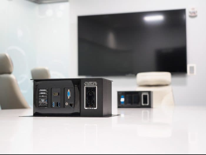 Conference table connectivity box with cables next to a wall-mounted display